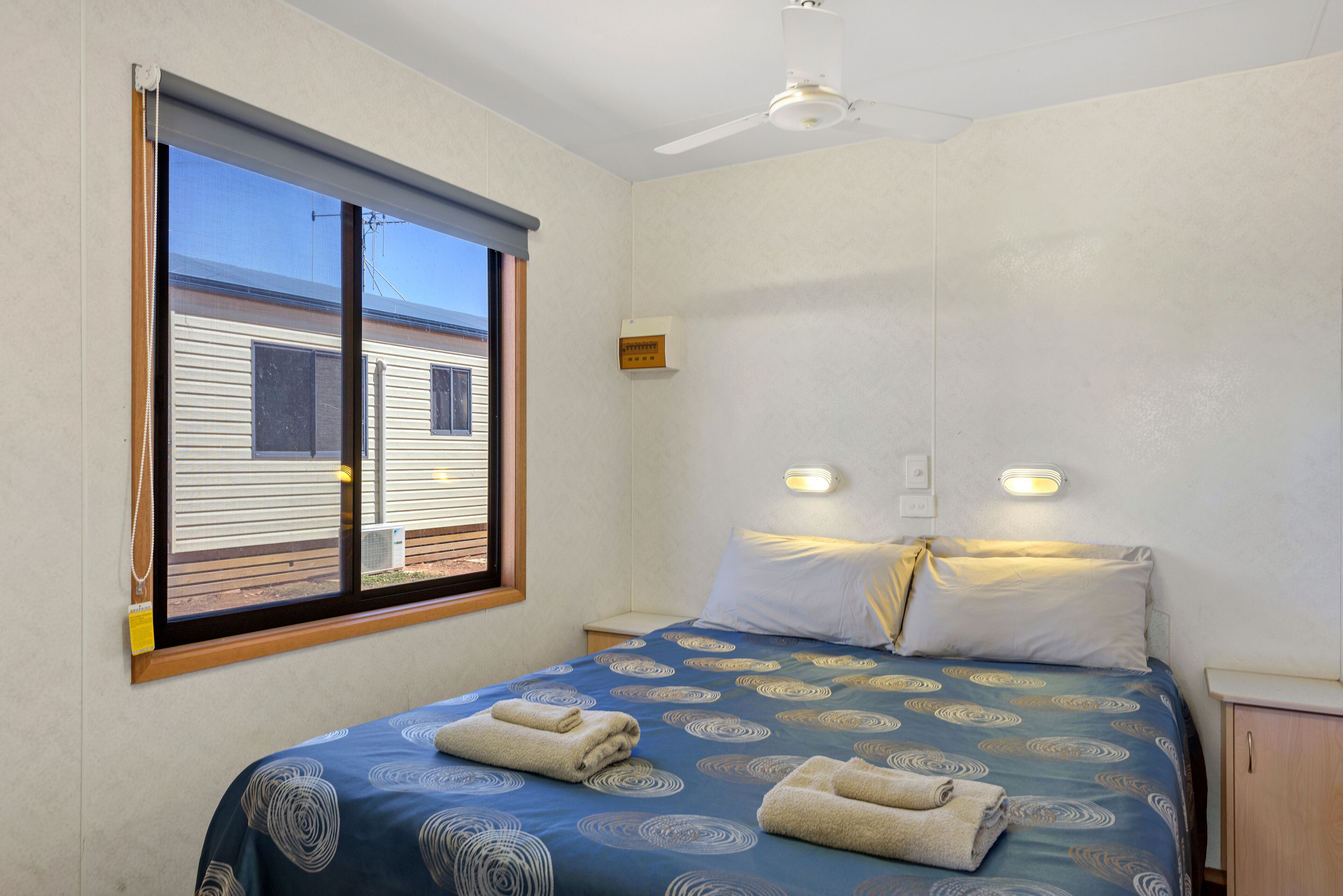 A bedroom with a bed, a window, a ceiling fan, and a wall-mounted light.