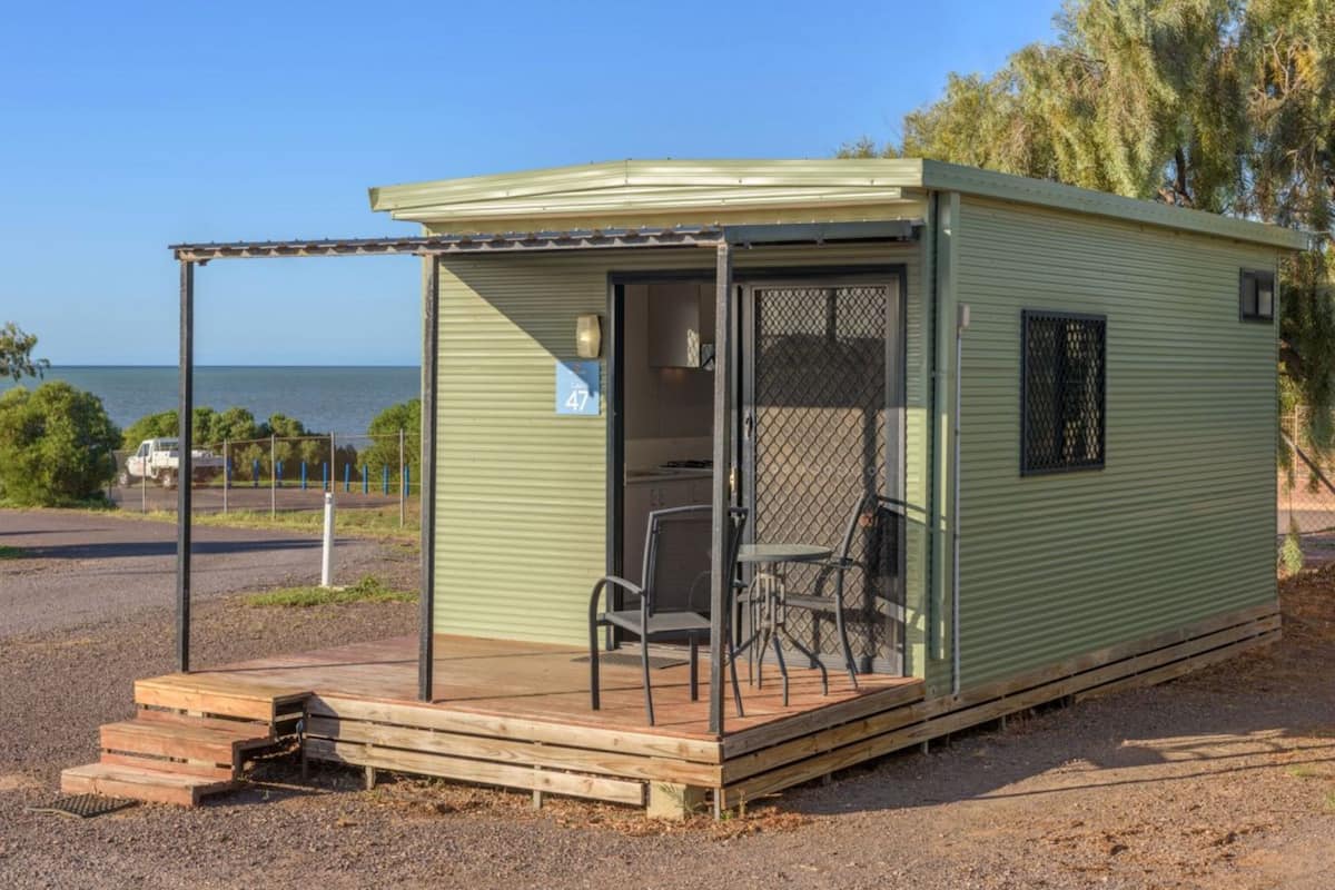 A small, single-story mobile home with a covered porch and a fenced patio area.
