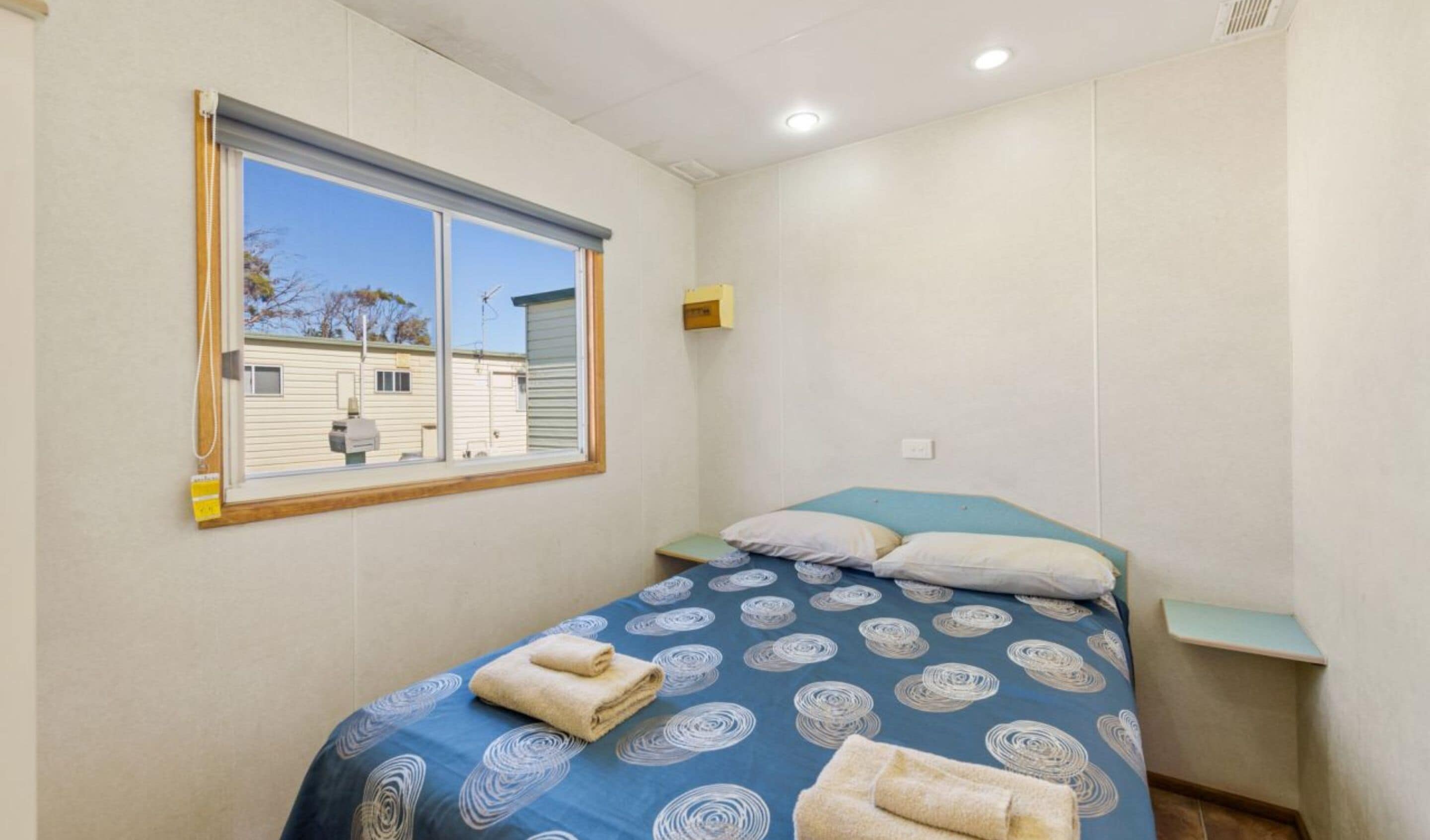A small, single-bed room with a window overlooking a residential area.