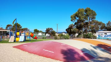 Une aire de jeux avec une surface rouge, des toboggans jaunes et verts, et une structure d’escalade.