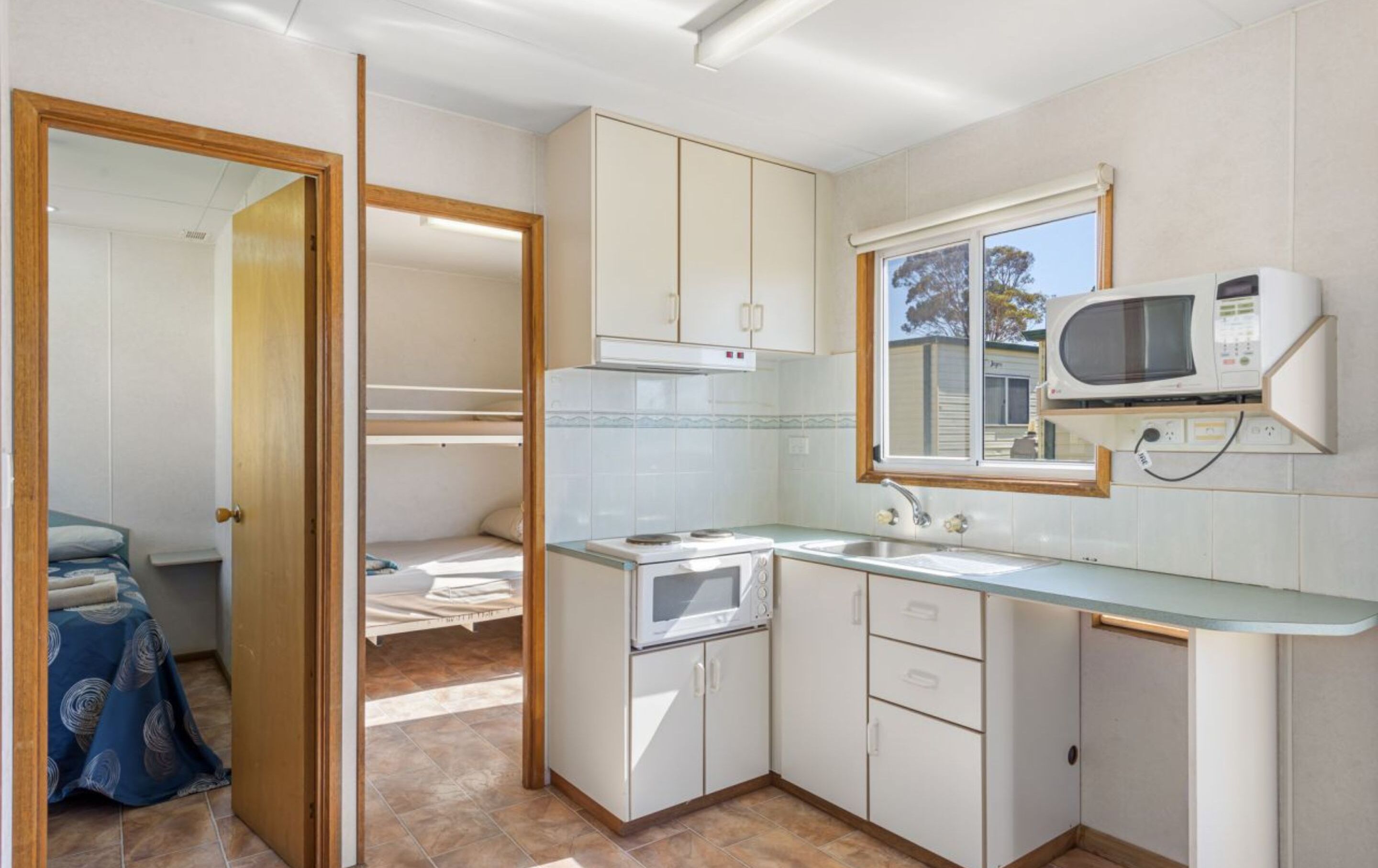 Cocina compacta con armarios blancos, microondas y ventana.
