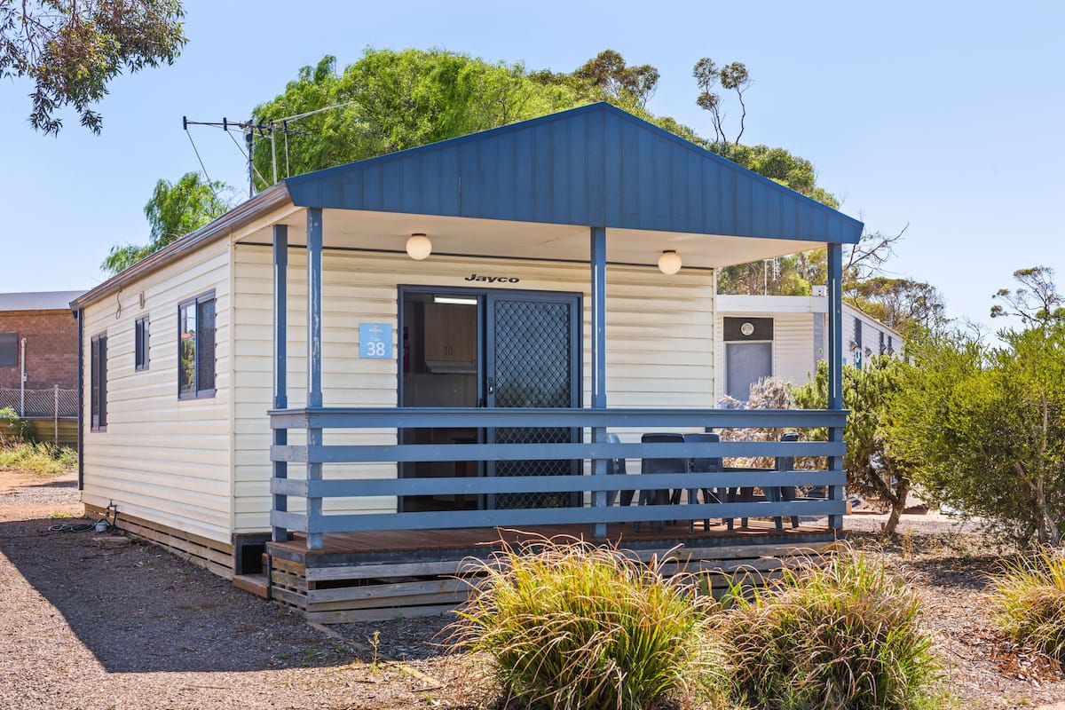 A small, single-story mobile home with a blue roof and a covered porch.