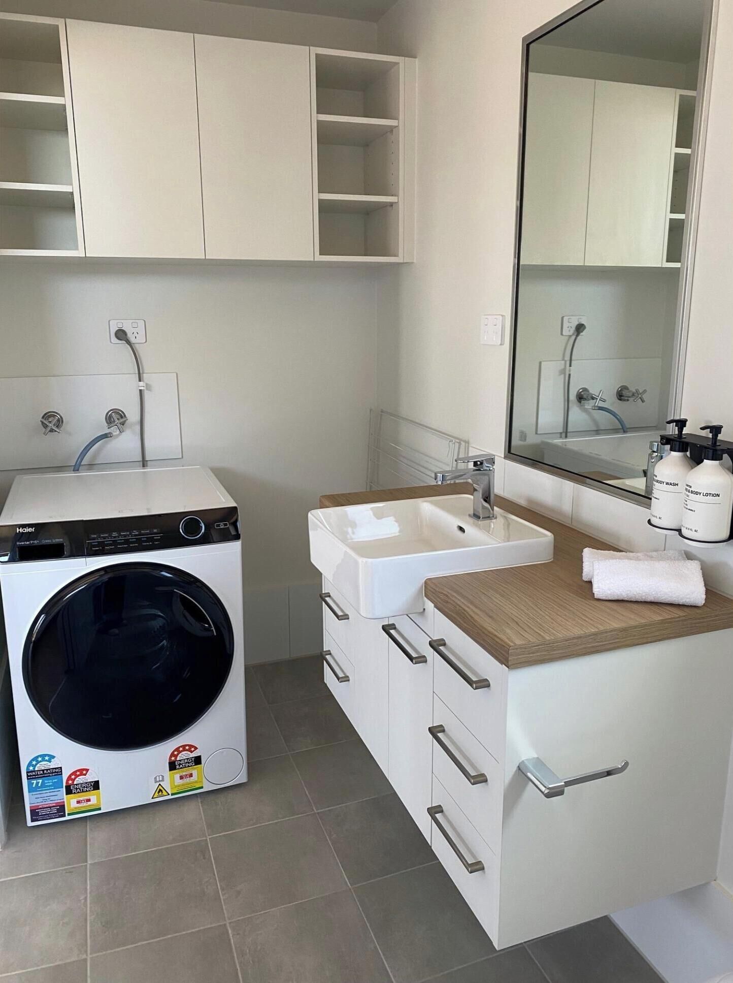 A compact bathroom with a front-loading washing machine, a sink, and a mirror.