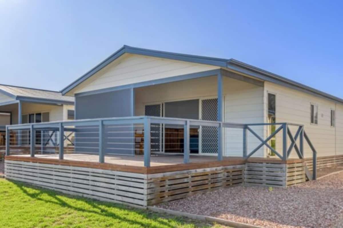 A modern mobile home with a covered porch and a fenced outdoor area.
