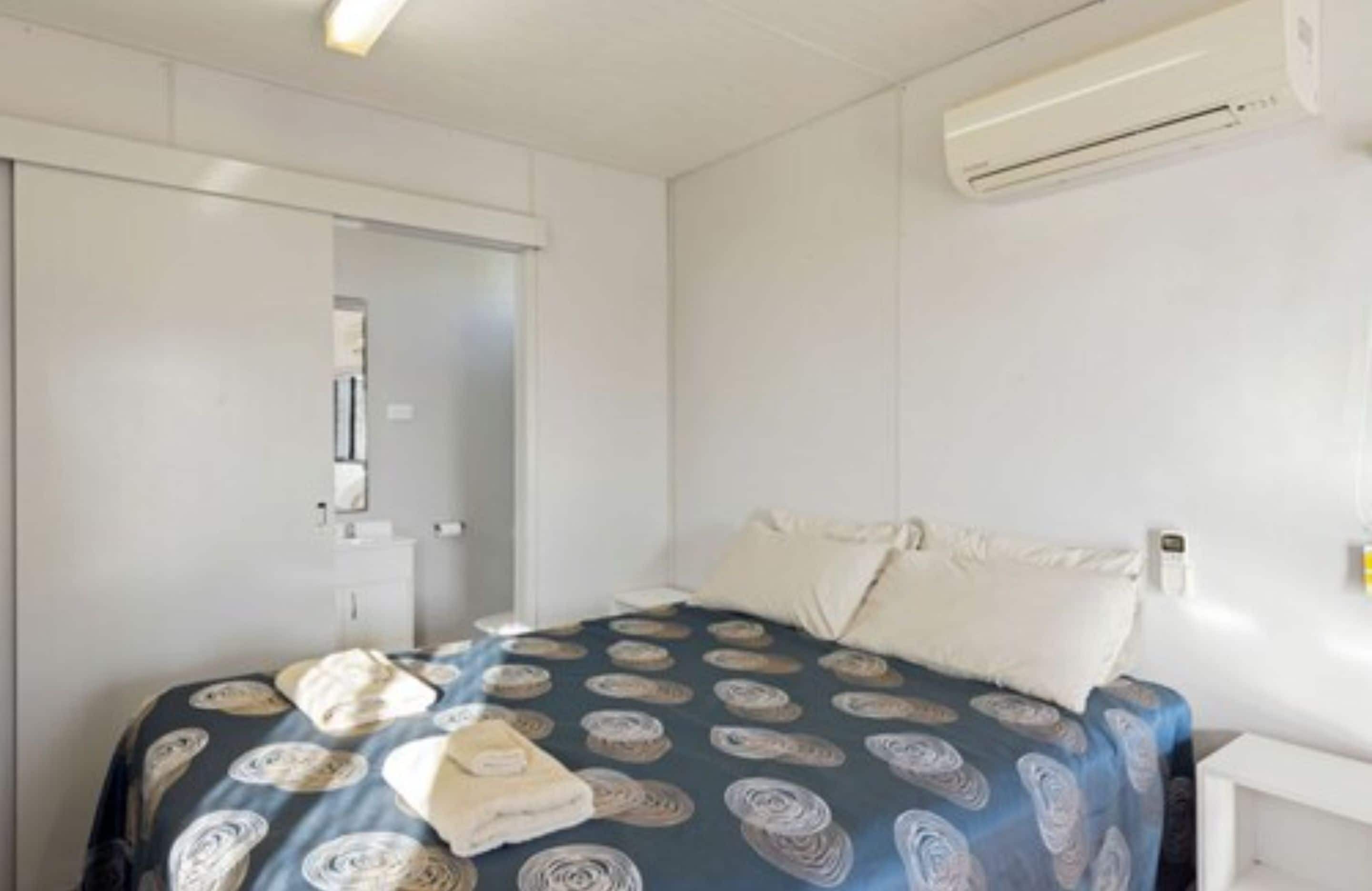 A bedroom with a bed, pillows, a bedside table, an air conditioning unit, and a door.