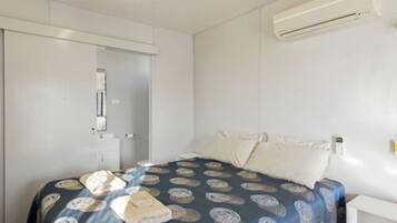 A bedroom with a bed, pillows, a bedside table, an air conditioning unit, and a door.
