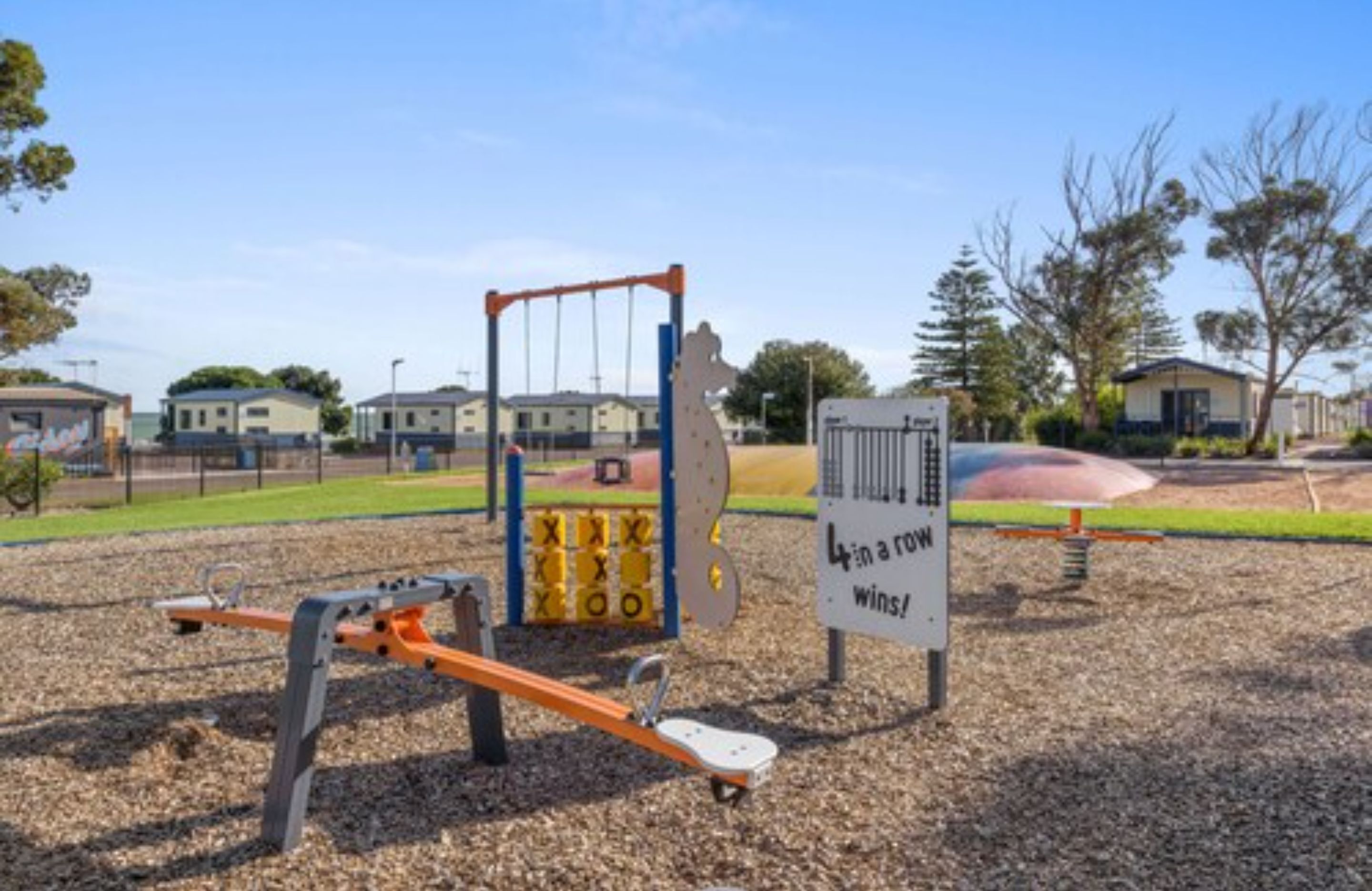 Un parque infantil con un sube y baja, una estructura para escalar y un cartel que dice '4 en línea gana'.