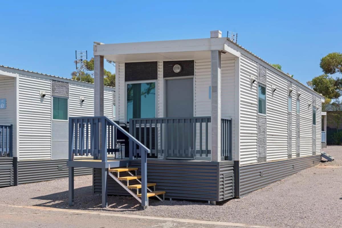 A modern mobile home with a covered porch, a staircase, and a window.