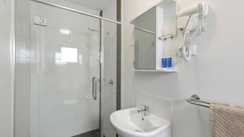 A modern bathroom with a glass shower enclosure, a white sink, a towel rack, and a hairdryer mounted on the wall.