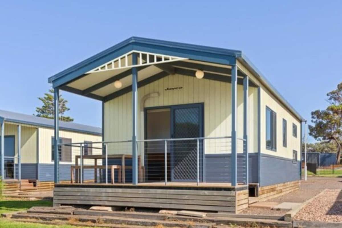 A single-story mobile home with a covered porch, a large window, and a door.