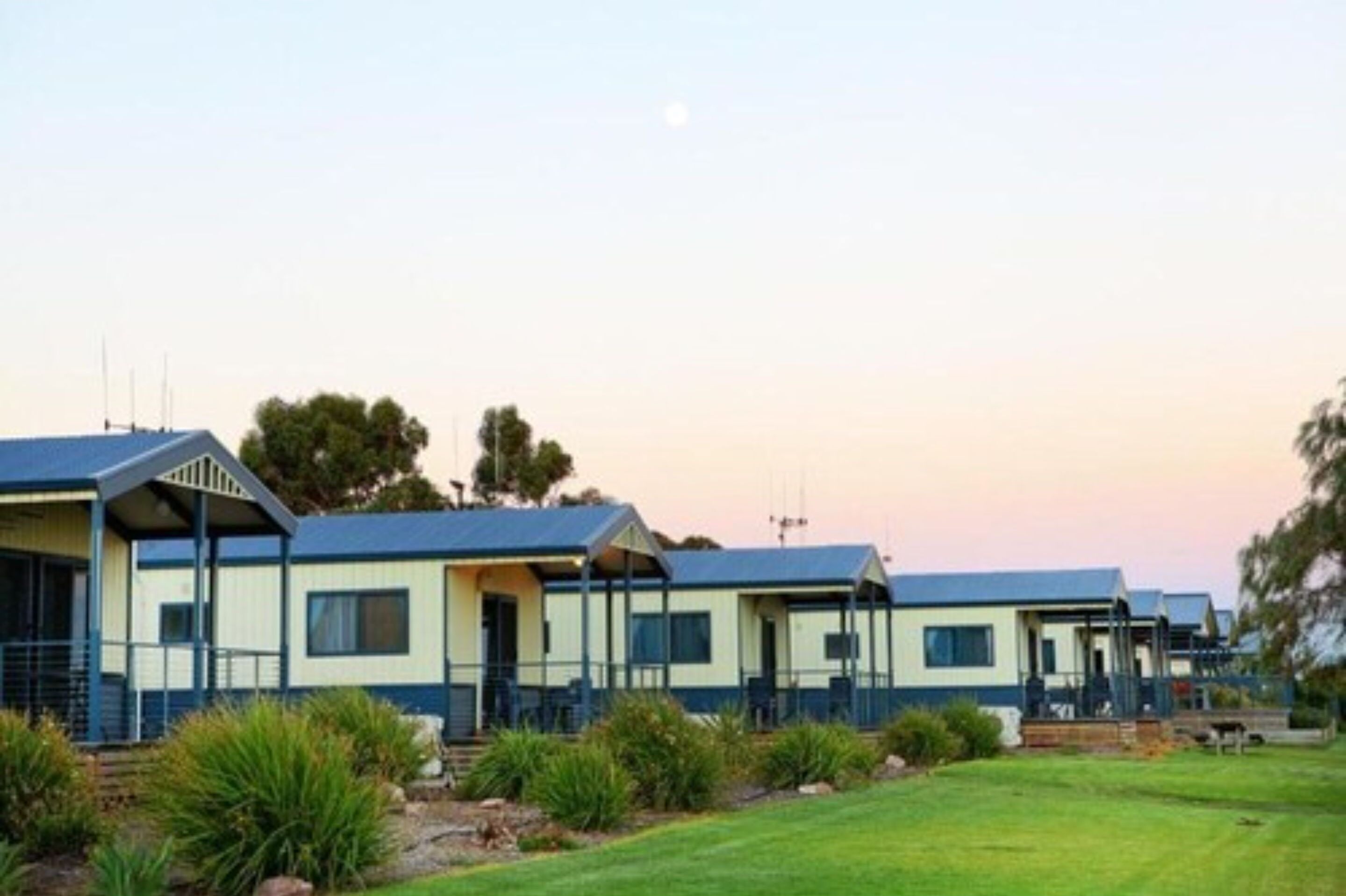 A row of mobile homes with a grassy lawn and trees in the background.