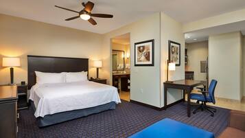 A hotel room with a bed, desk, chair, and a ceiling fan.