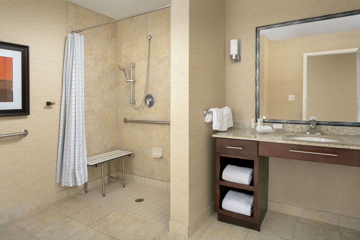 Un baño de hotel con ducha, un banco, un lavabo y un espejo.