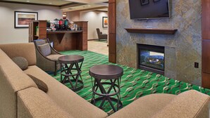Un hall de hotel con un sofá, dos taburetes de bar, una chimenea, un televisor y una estación de café.