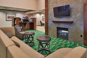 Un hall de hotel con un sofá, dos taburetes de bar, una chimenea, un televisor y una estación de café.