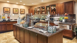 Una cocina de hotel con un mostrador tipo bufé, armarios de madera y diversos electrodomésticos.
