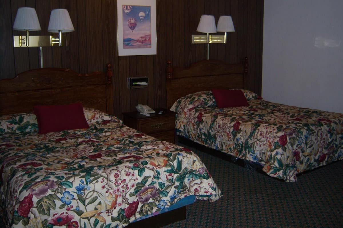 A hotel room with two beds, each with floral bedding and a red pillow. There are two wall-mounted lamps and a framed picture on the wall.