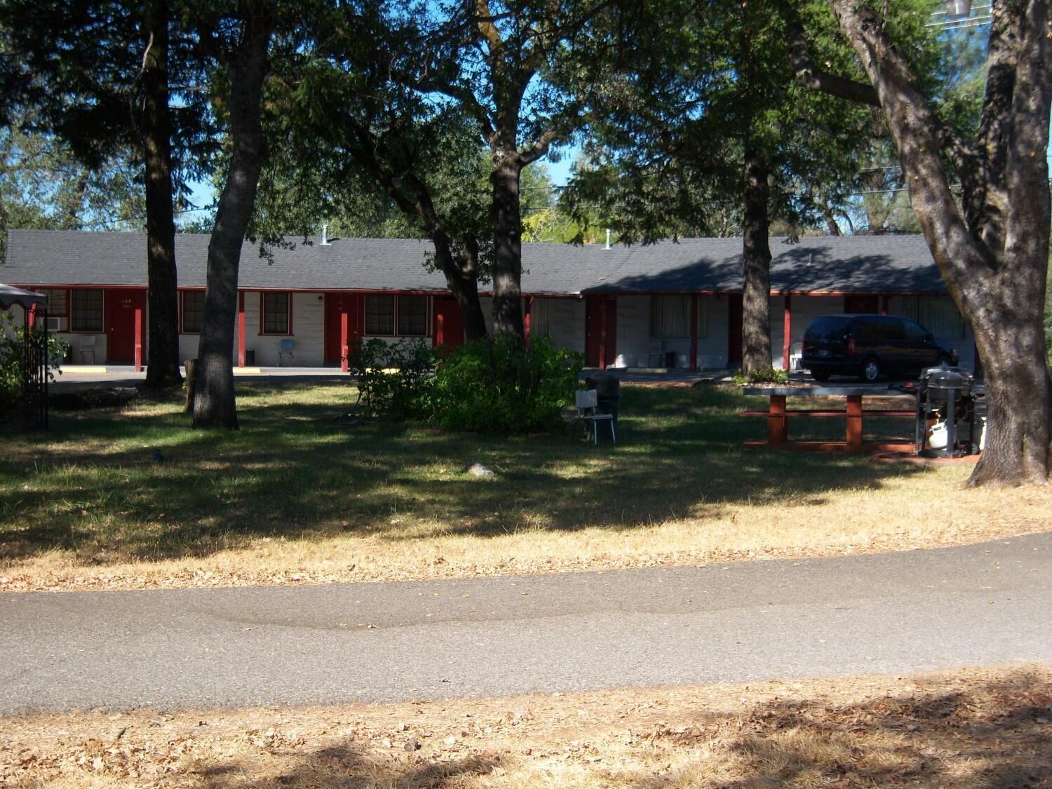 A row of motel buildings with red doors and windows, surrounded by trees and a parking area.