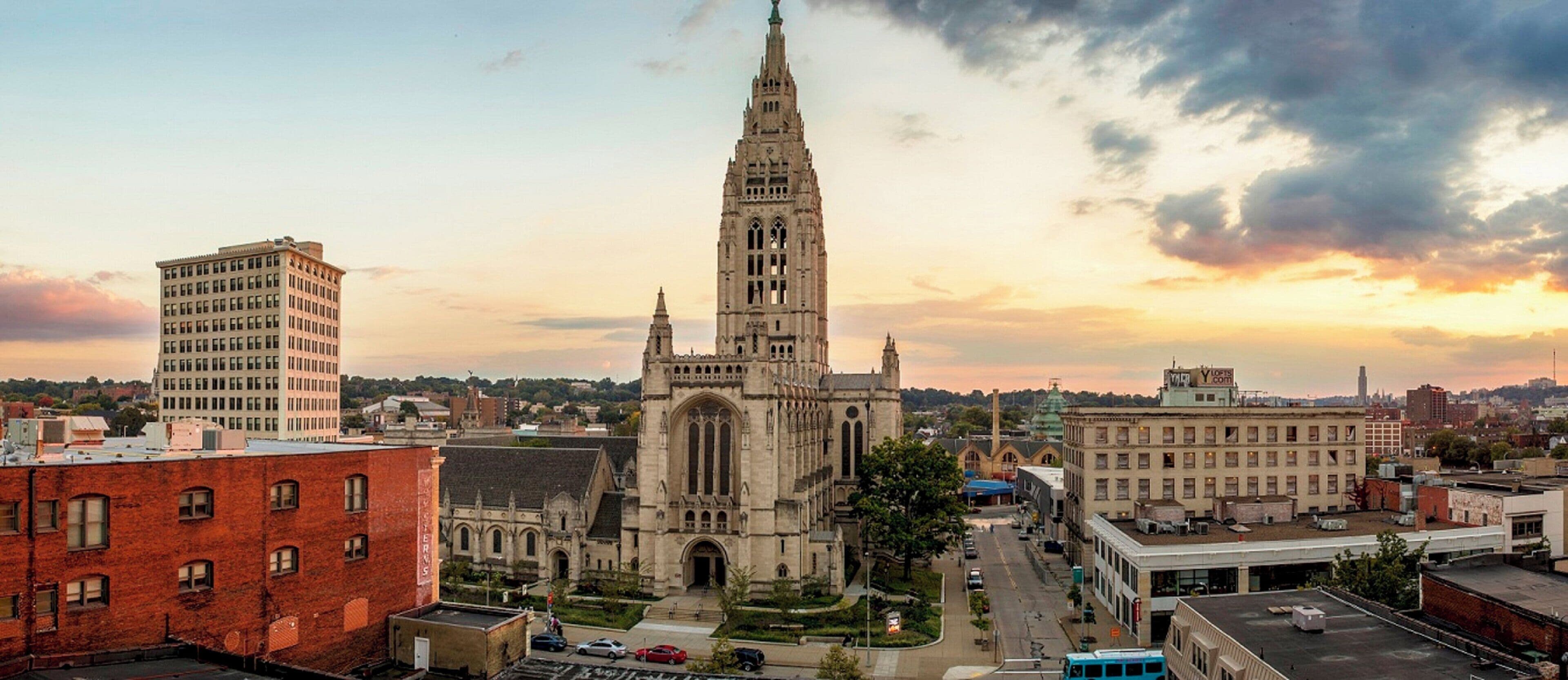 A historic building with a tall tower, surrounded by modern buildings and a clear sky.
