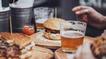 Uma refeição com hambúrguer, sanduíche, um copo de cerveja e um pote de molho sobre uma mesa.
