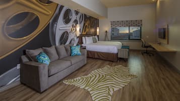 A modern hotel room with a large bed, a sofa, a zebra rug, and a cityscape view.