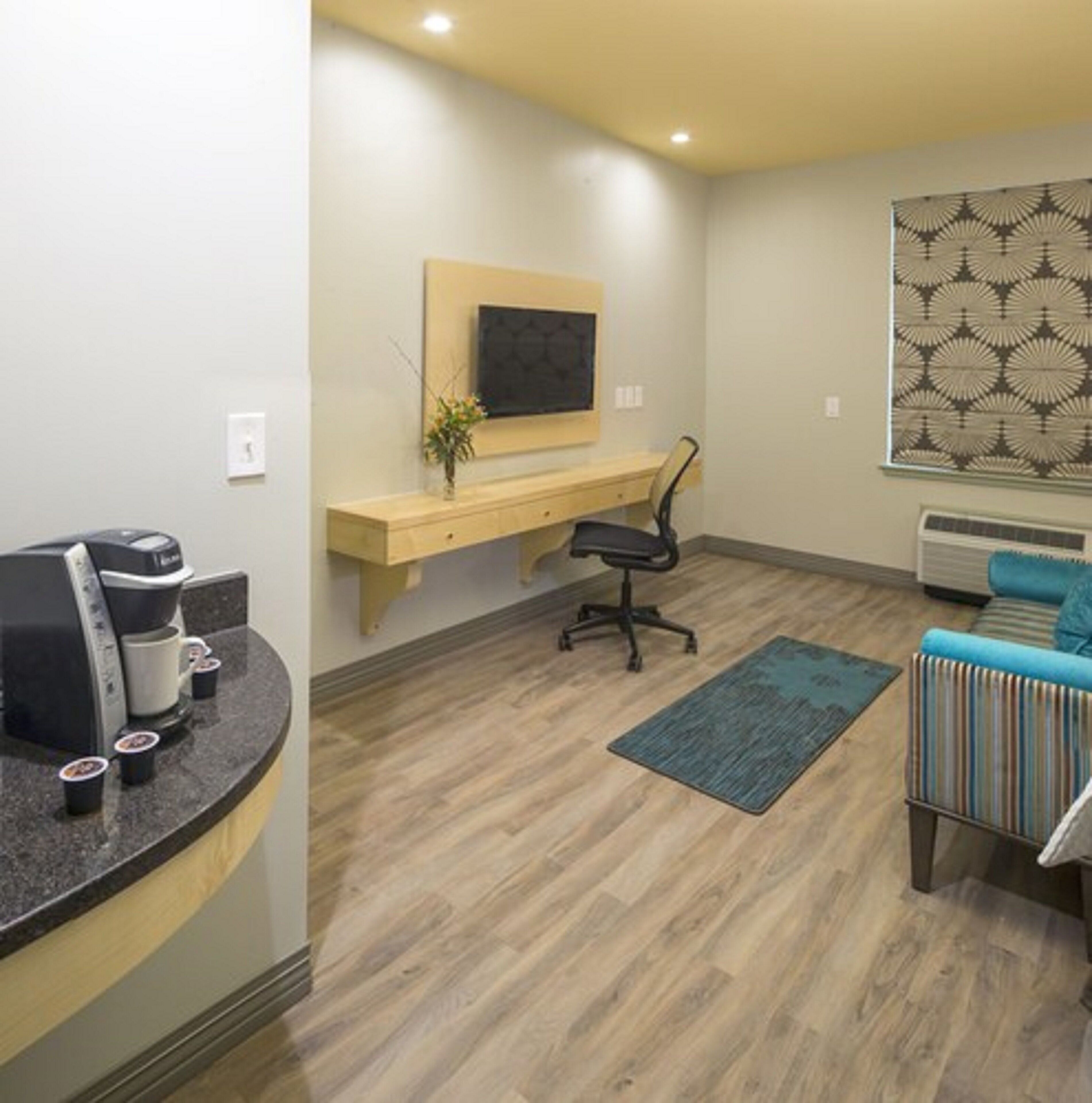 A modern room with a wooden floor, a desk with a chair, a coffee maker, a blue rug, and a blue sofa.
