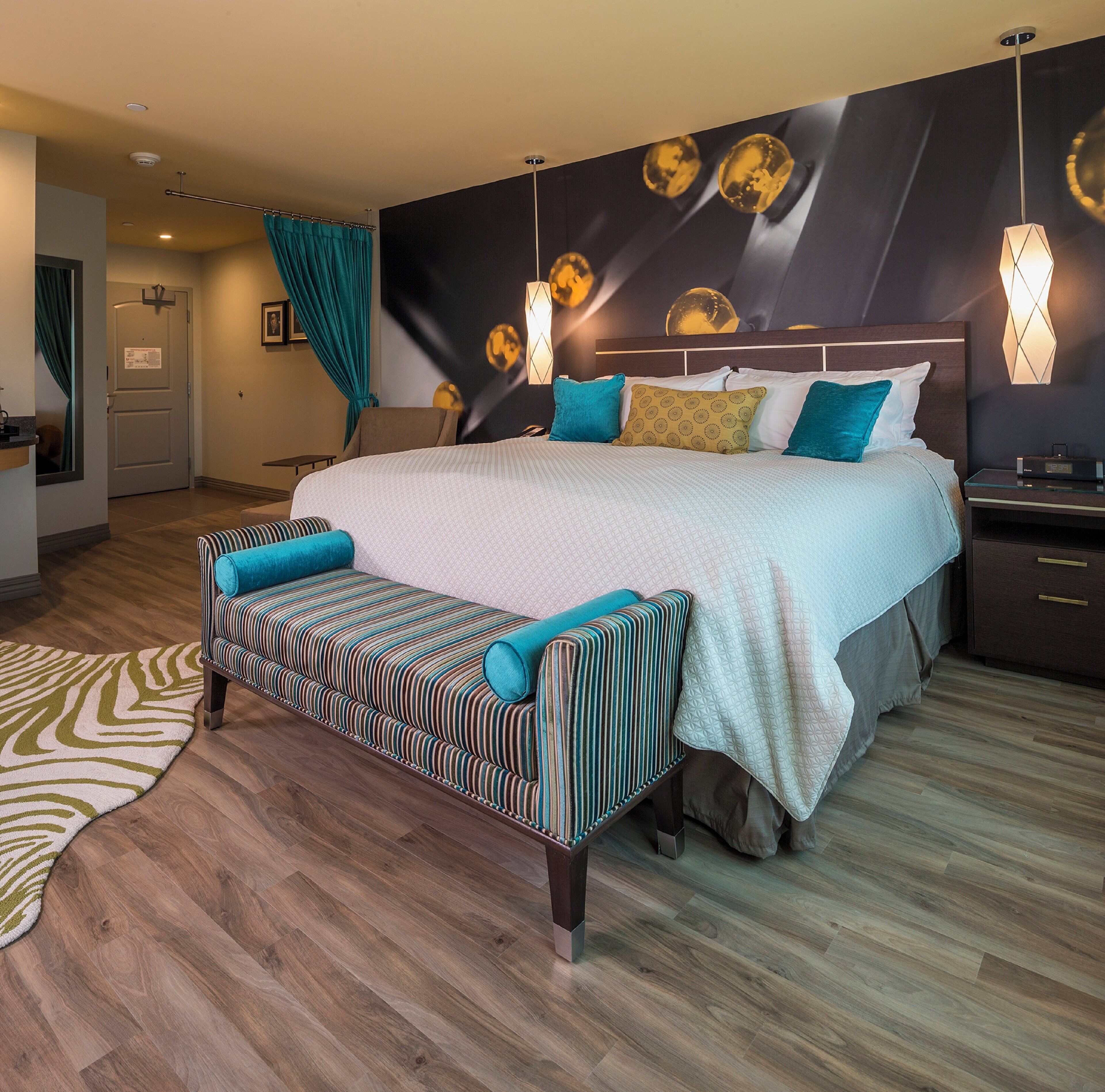 A modern hotel room with a large bed, a bench, a nightstand, and a wall-mounted lamp.