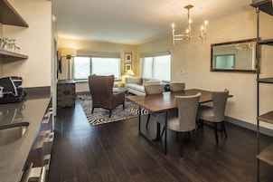 A modern kitchen with a built-in dishwasher, a dining area with a wooden table and chairs, and a living room with a sofa and a lamp.