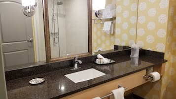 Une salle de bain équipée d’un lavabo, d’un miroir, d’un porte-serviettes, d’une douche et d’un rouleau de papier toilette.