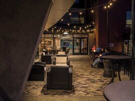 An outdoor seating area with wicker furniture and string lights, leading to a building entrance.
