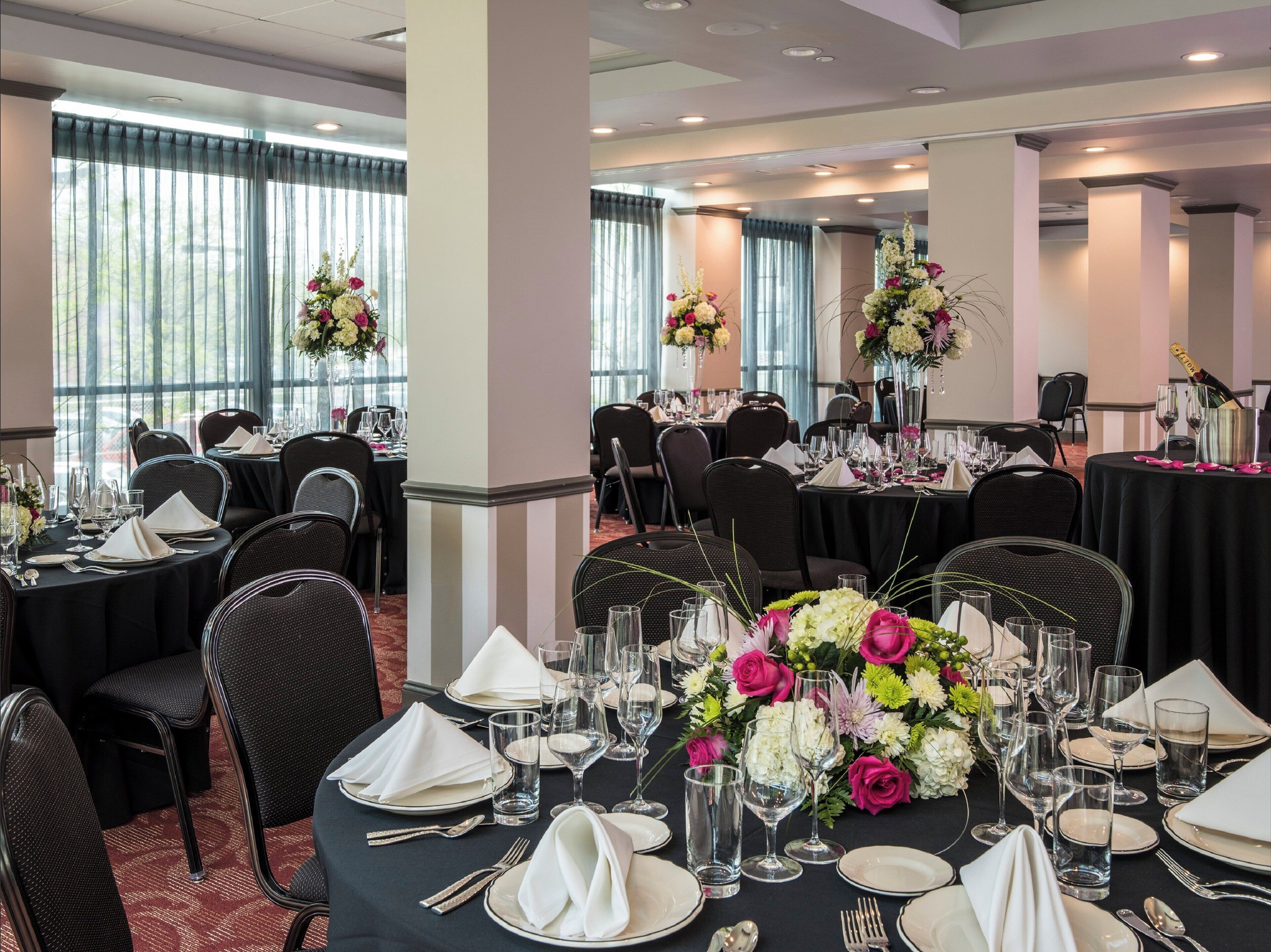 A banquet hall with round tables set for dining, each with white napkins, plates, and cutlery.