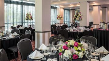A banquet hall with round tables set for dining, each with white napkins, plates, and cutlery.