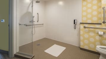 A bathroom with a glass shower enclosure, a toilet, and a handrail.
