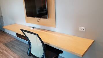 A modern office space with a wooden desk, a black office chair, and a mounted flat-screen TV.