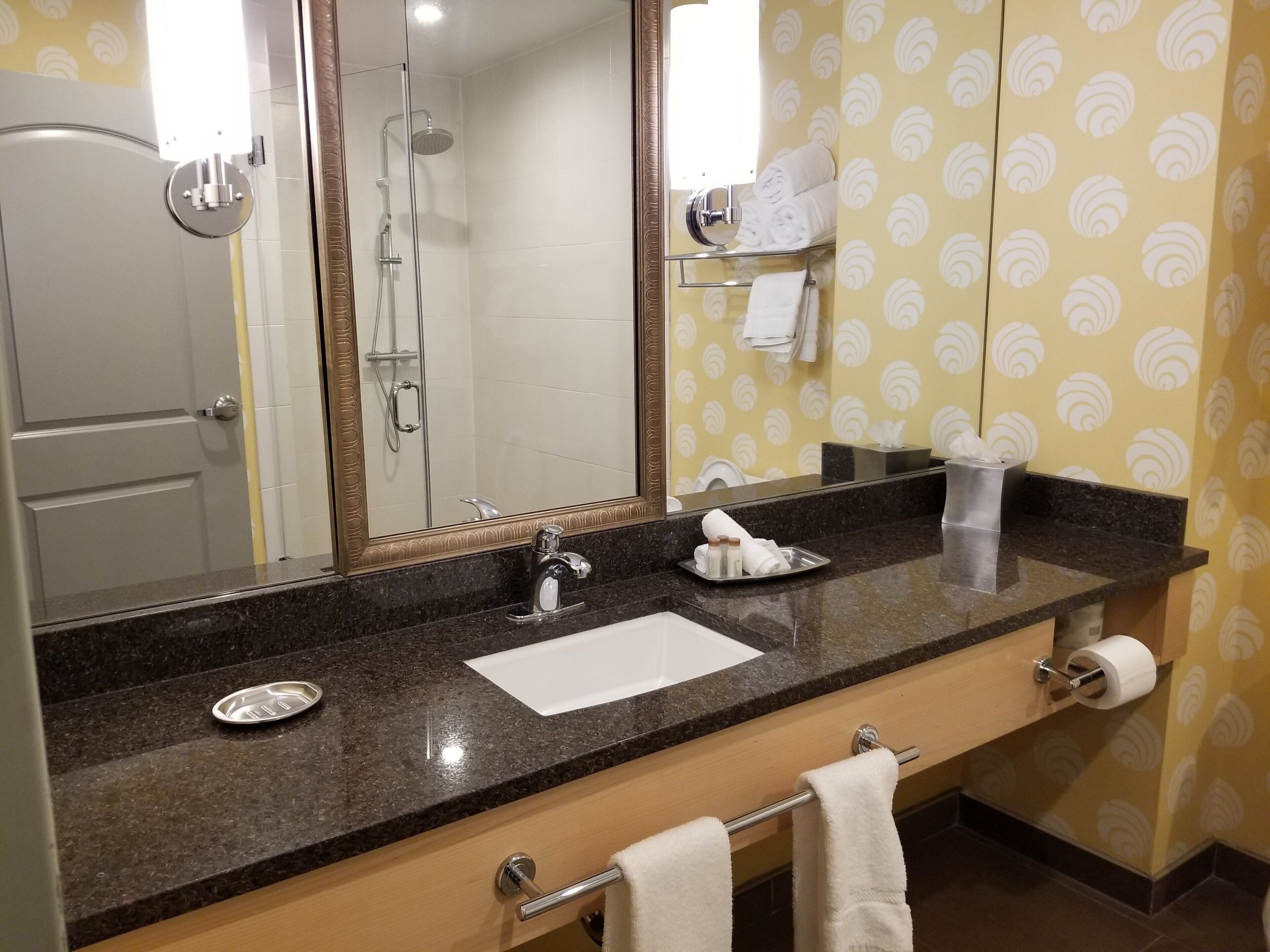 A bathroom with a sink, mirror, towel rack, and shower.