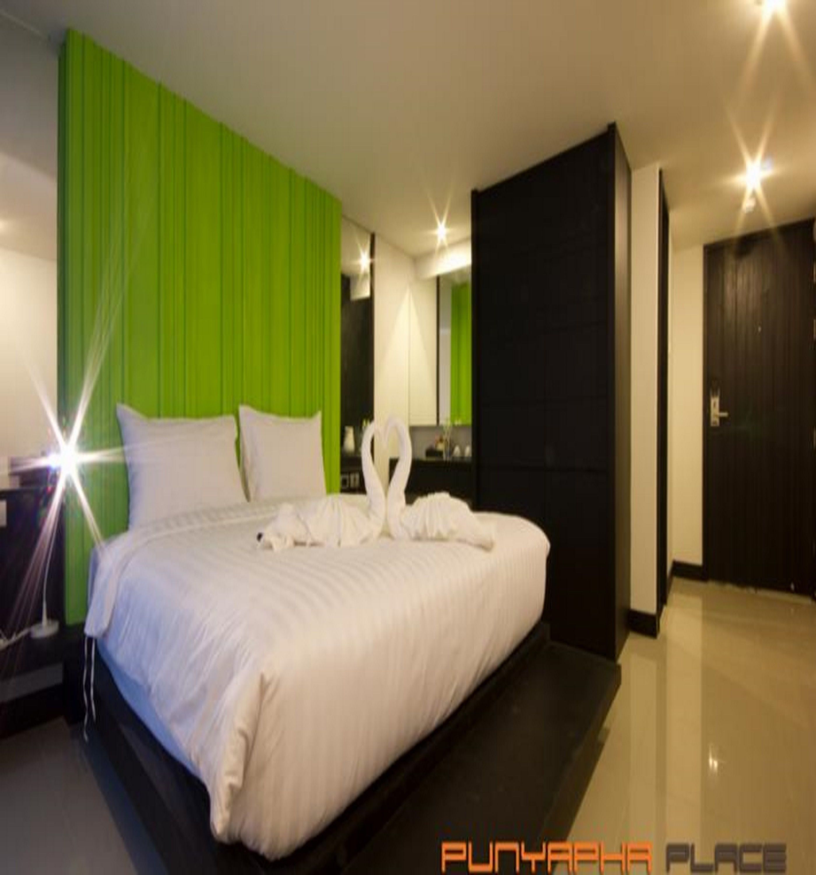 A modern hotel room with a large bed, green accent walls, and a black wardrobe.
