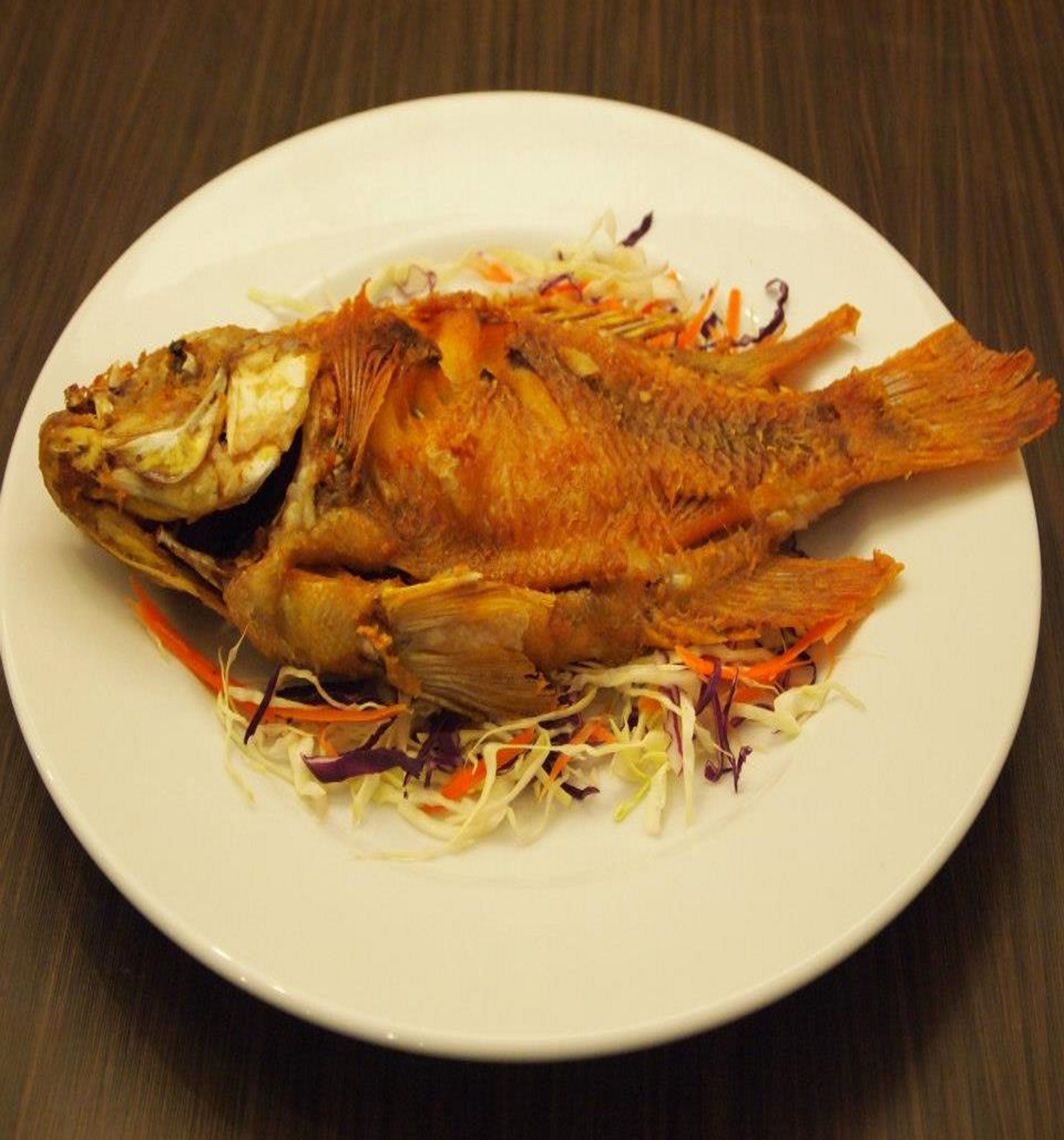 A whole fried fish on a white plate with a side of shredded vegetables.