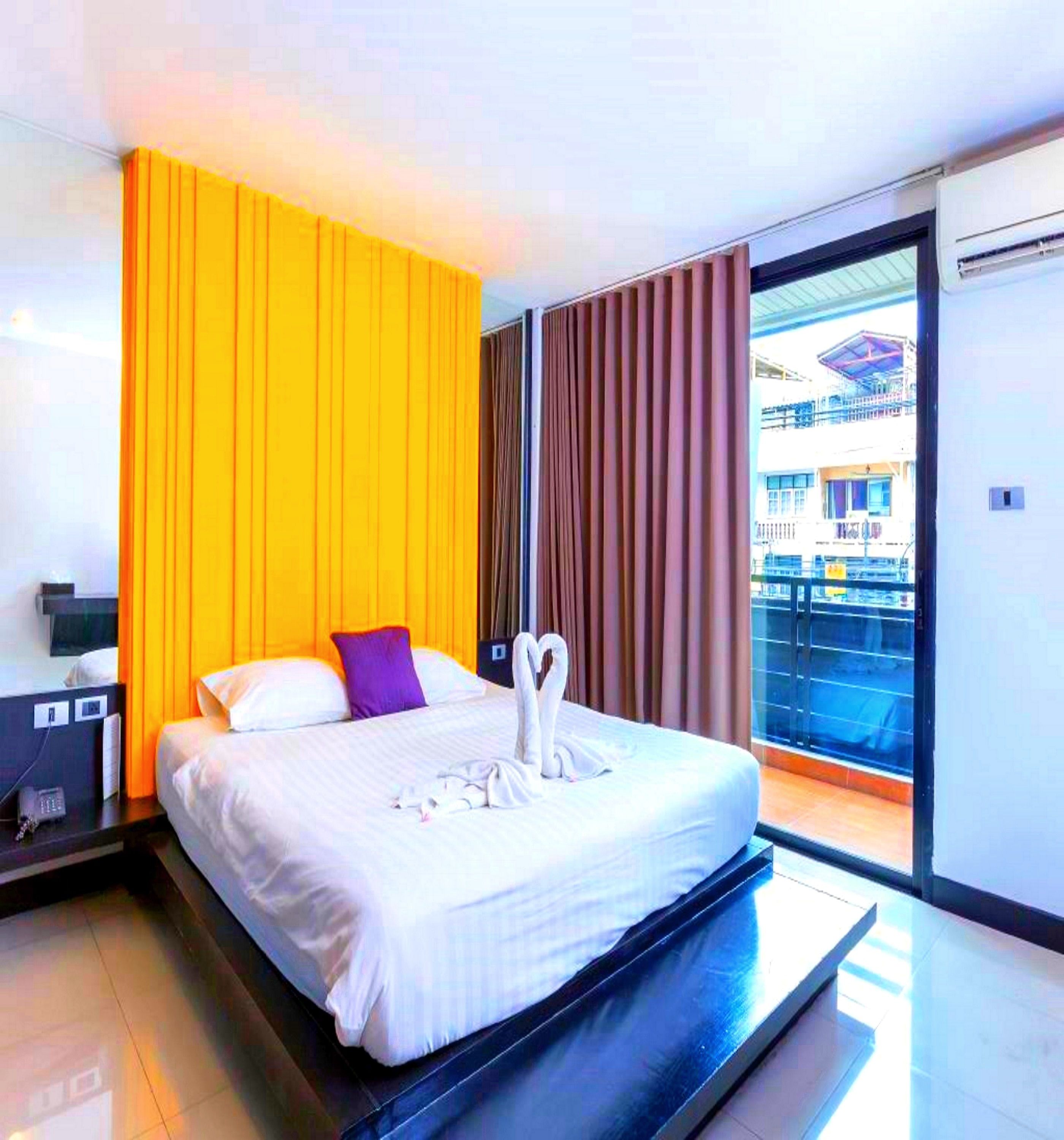 A modern hotel room with a large bed, a nightstand, a telephone, and a view of the city through a large window.