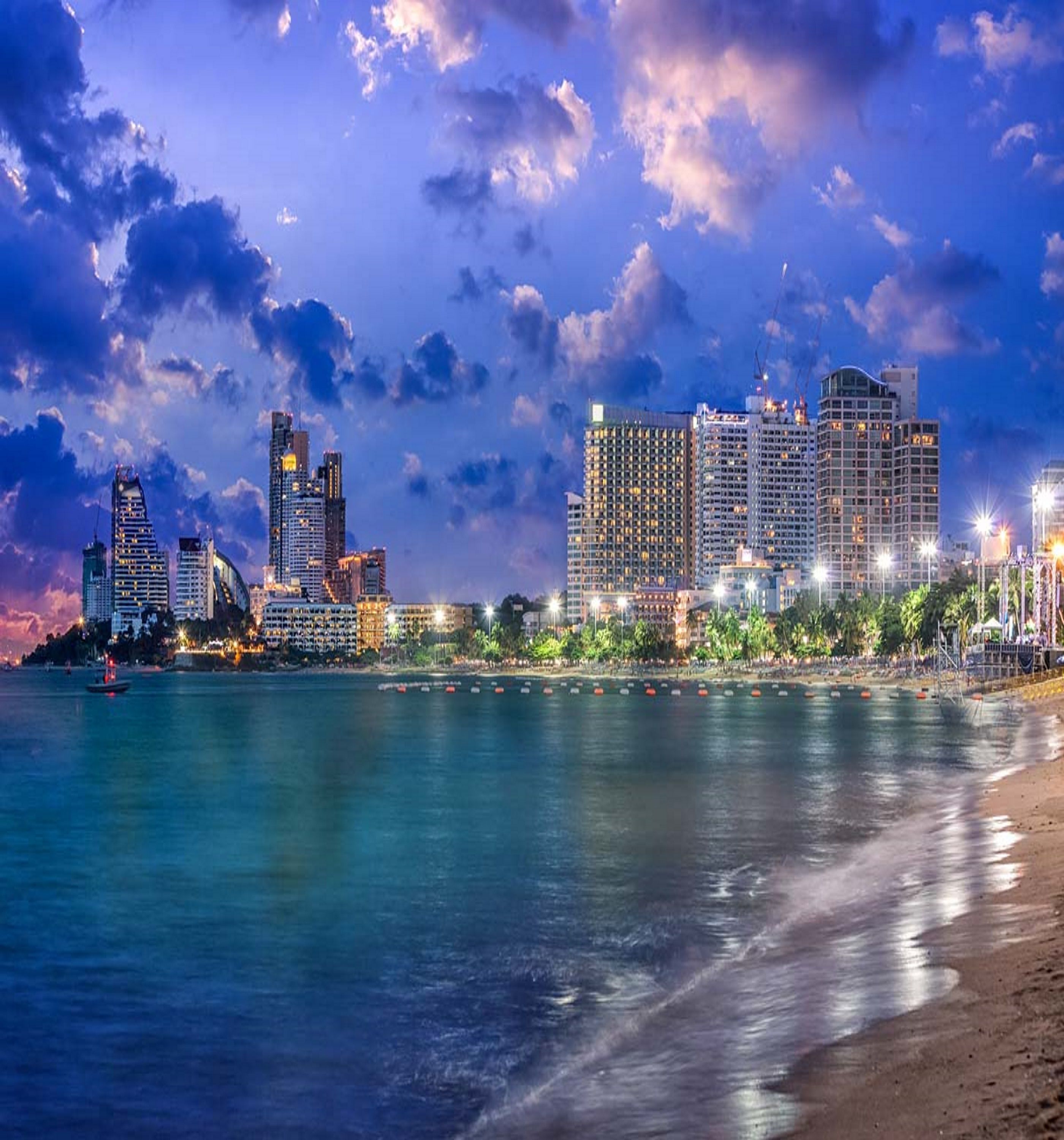 Un paysage urbain côtier au crépuscule, avec des bâtiments illuminés et une mer calme.