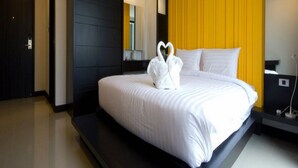 Una habitación de hotel moderna con una cama grande, un armario negro, una pared de acento amarilla y un arreglo de toallas blancas con forma de corazón.