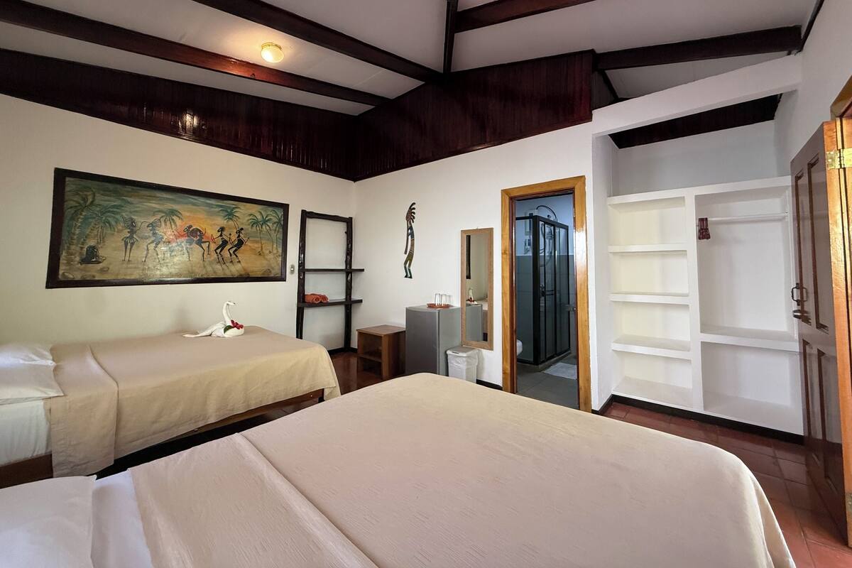 A hotel room with two beds, a painting, a mirror, a wardrobe, and a door leading to a bathroom.