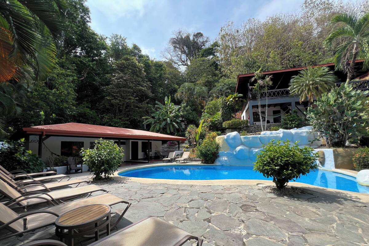 A pool area with lounge chairs, a small building, and a waterfall feature.