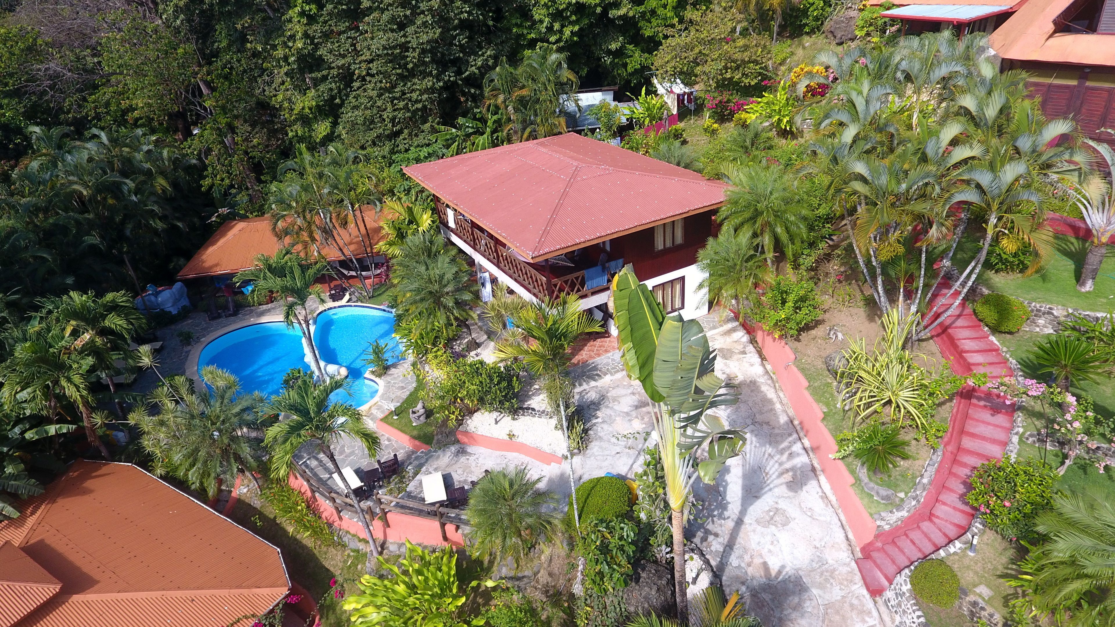 A resort with a swimming pool, a red-roofed building, and lush greenery.
