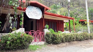 A building with a sign reading "Cabañas Jardin." It features a red roof, a stone base, and a red gate. - Hotel El Jardín (Cóbano)