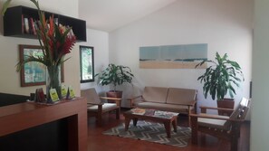 A living room with a sofa, chairs, a coffee table, a bookshelf, and potted plants. - Hotel El Jardín (Cóbano)