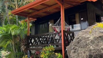 A covered outdoor area with a wooden bench, a hammock, and a large rock.