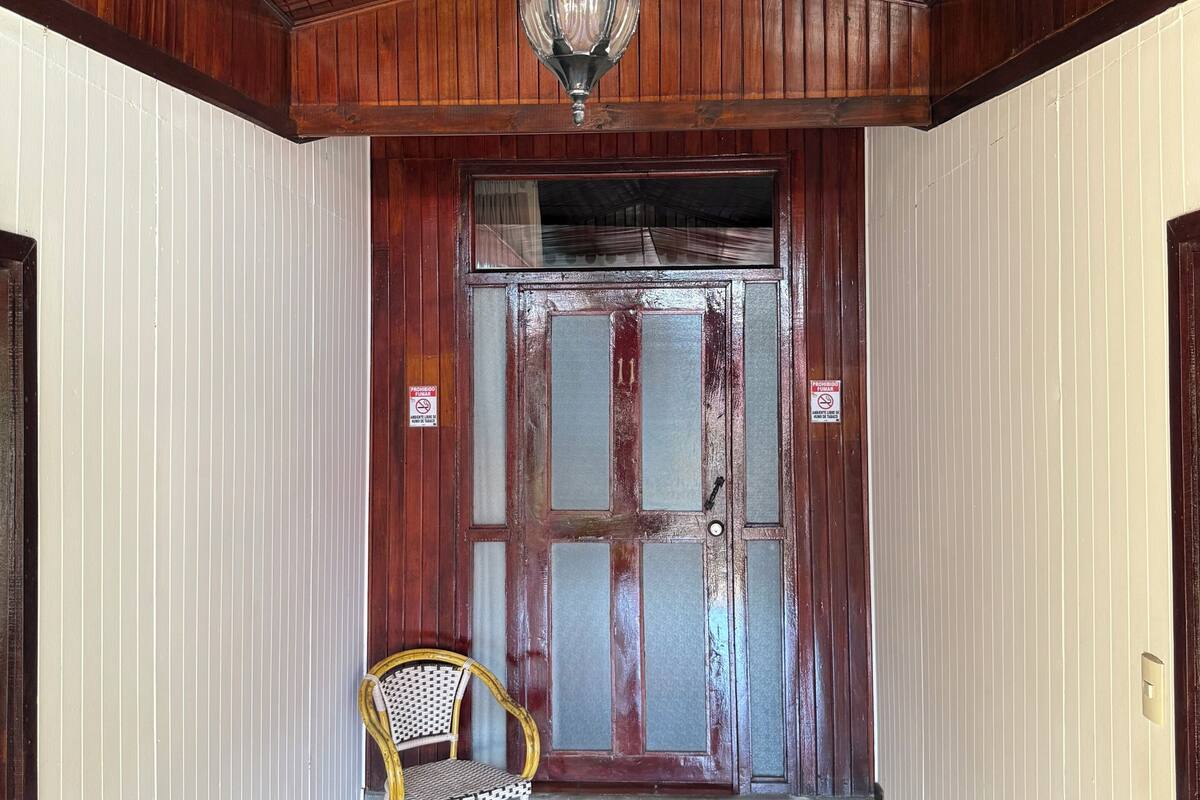 A hallway with wooden paneling, a hanging light fixture, a door with a sign, and a chair.