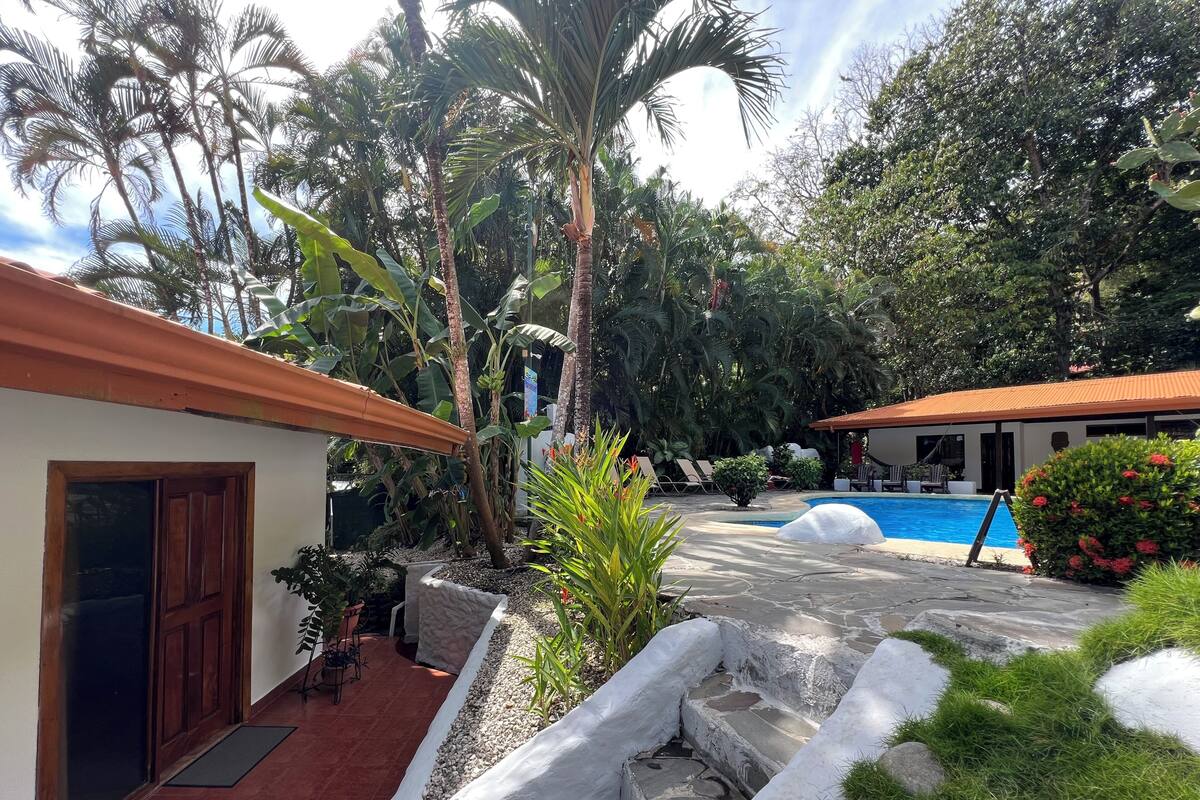A pool area with a tiled deck, palm trees, and a building with a red roof.