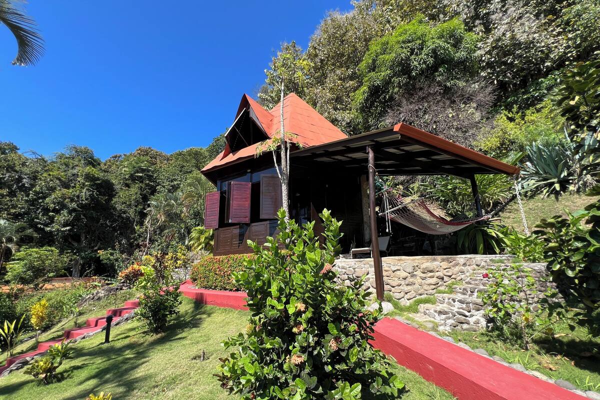 A house with a red roof, a hammock, and a stone wall.