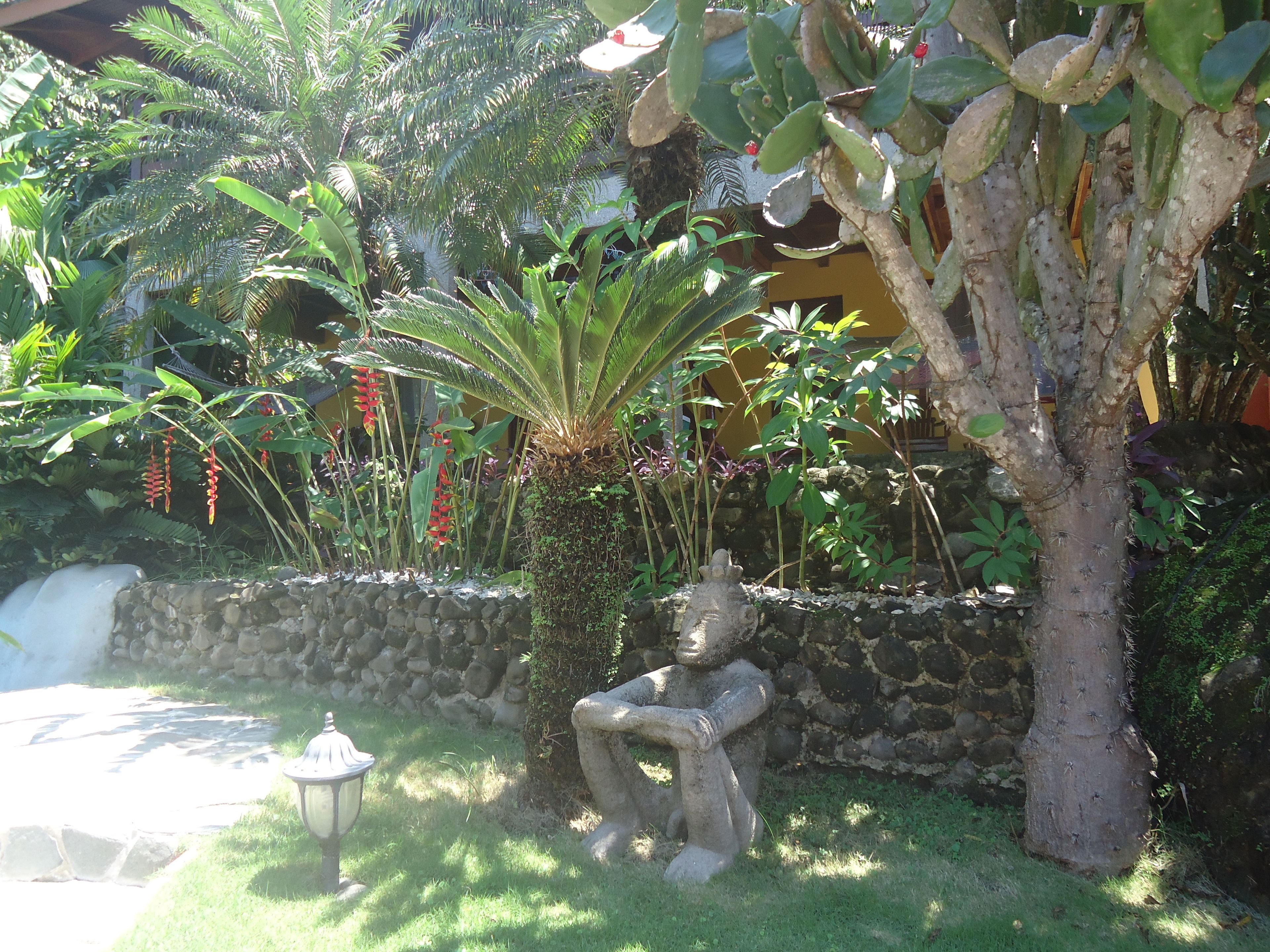 A garden with a stone wall, a statue, and various tropical plants.